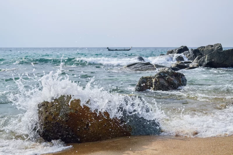 Волны разбиваются о скалы на песчаном пляже