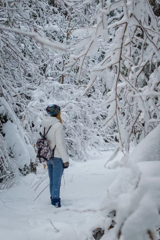 Женщина с рюкзаком в заснеженном зимнем лесу