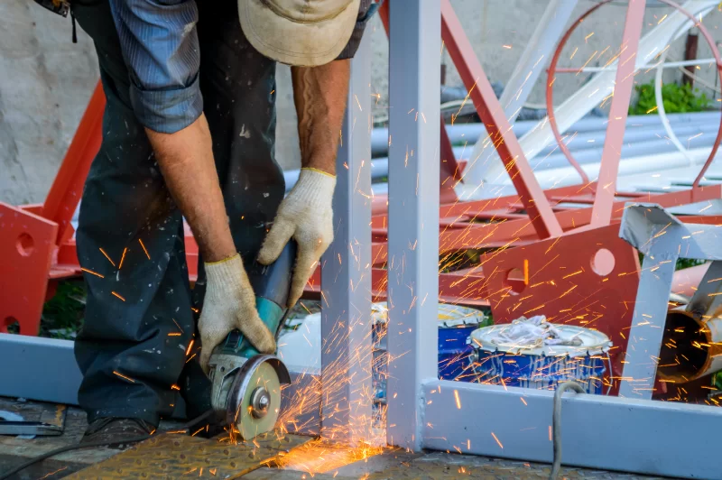 Рабочий шлифует металлическую конструкцию угловой шлифмашиной, искры летят во все стороны