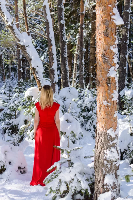 Девушка в красном платье в зимнем лесу, окруженная снегом и елями