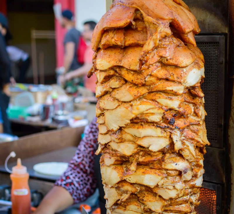 Сочный вертикальный гриль с курицей для шаурмы на фоне уличного кафе