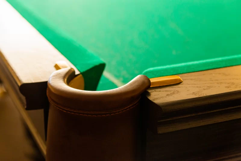 Детальный кадр бильярдного стола с зеленым сукном и кожаными подлокотниками