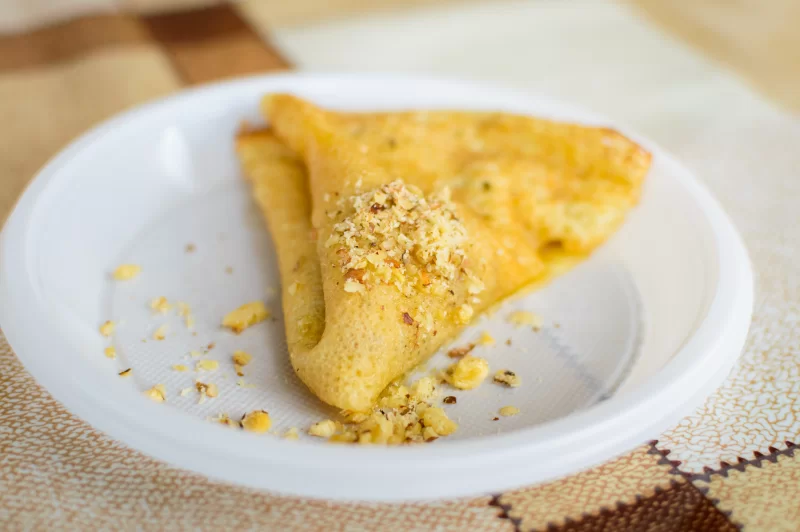 Золотистый блинчик с ореховой крошкой на белой тарелке