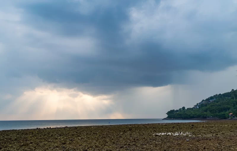 Солнечные лучи пробиваются сквозь тёмные облака над побережьем