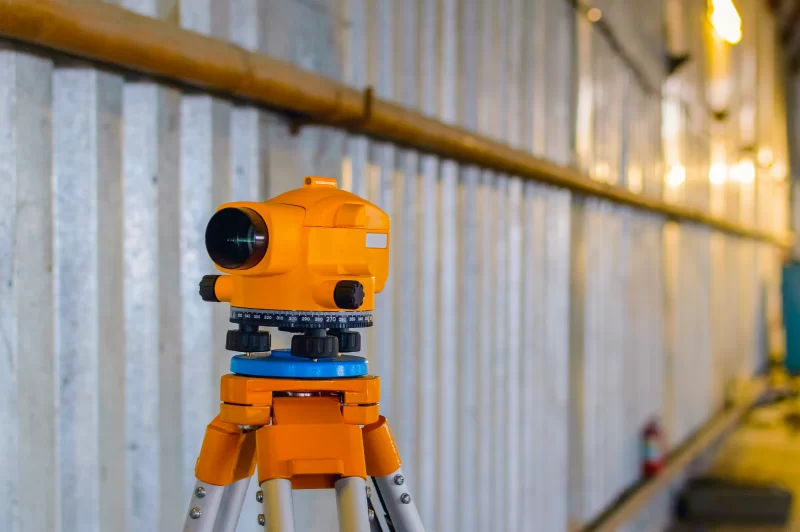 Точный нивелир на штативе на фоне промышленной стены