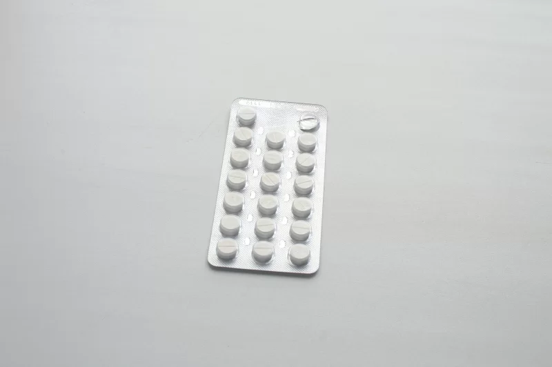 Блистер с белыми таблетками на сером фоне