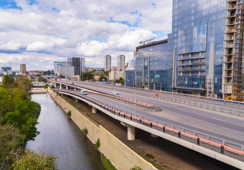 Современный городской пейзаж с автодорогой над рекой и стеклянными небоскрёбами