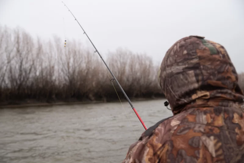 Рыбак в камуфляже ловит рыбу на реке в туманный день