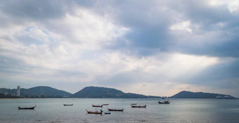 Солнечные лучи пробиваются сквозь облака над спокойным морем с лодками