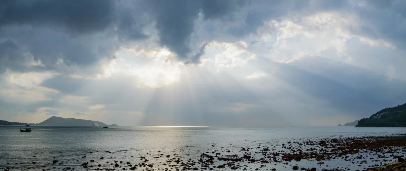 Солнечный свет пробивается сквозь тучи над спокойным морем