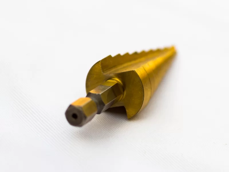 Золотая ступенчатая сверло для металла на белом фоне