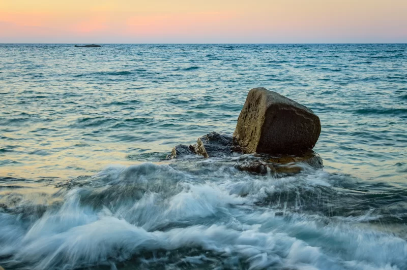 Разбившаяся волна у камня на закате