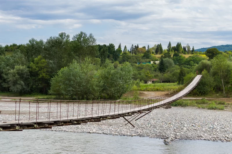 Веревочный подвесной мост через живописную реку в зеленом лесу