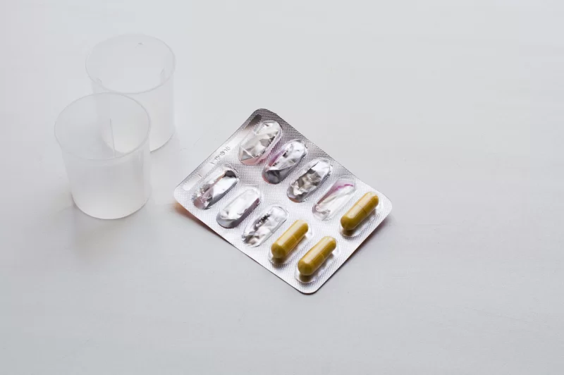 Упаковка капсул и мерные стаканчики на светлом фоне