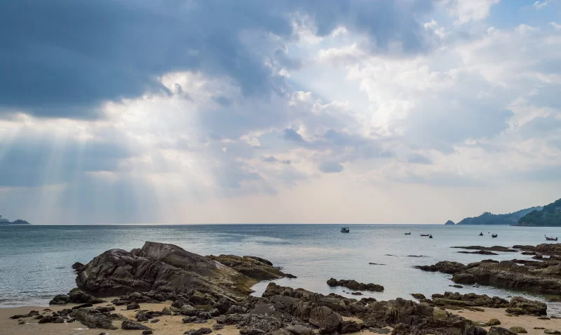 Sunlight beams through storm clouds over rocky coastline