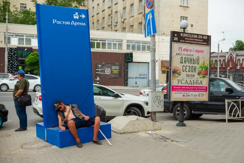 Homeless man rests near stadium sign in Rostov-on-Don