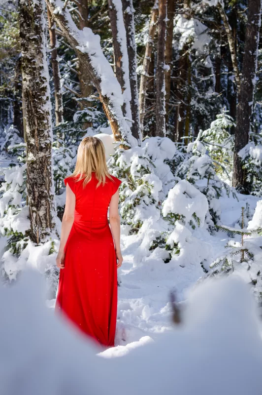 Элегантная блондинка в алом платье среди заснеженных деревьев