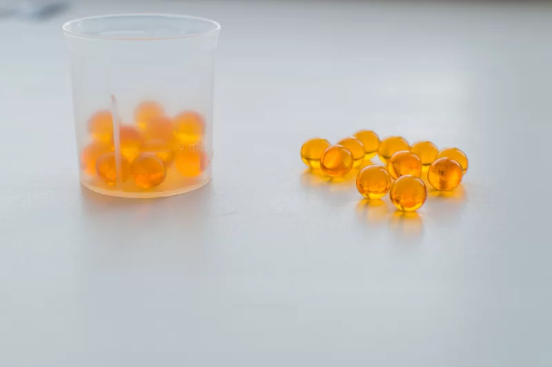 Яркие капсулы витамина D в мерном стаканчике и россыпью