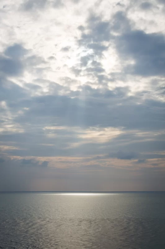 Солнечные лучи пробиваются сквозь тучи над спокойным океаном