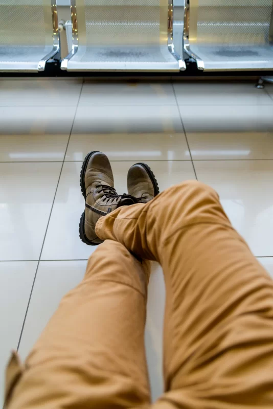 Ожидание в аэропорту: ноги в коричневых ботинках и брюках на фоне сидений