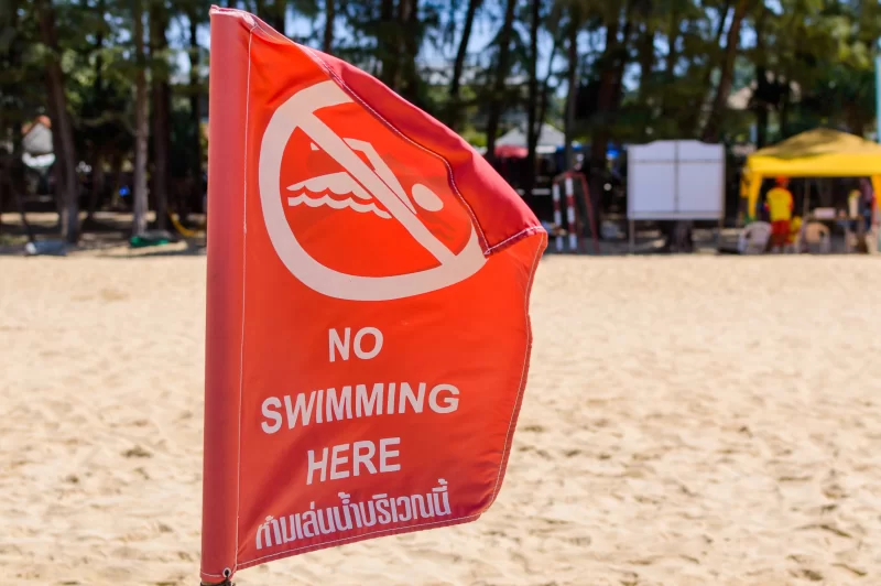 Красный флаг «Запрещено купаться» на пляже в солнечный день