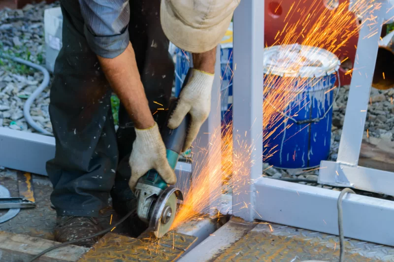 Рабочий шлифует металл угловой шлифмашиной, создавая фейерверк искр