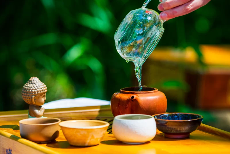 Церемония чаепития: вода льется в чайник, украшенный статуэткой Будды