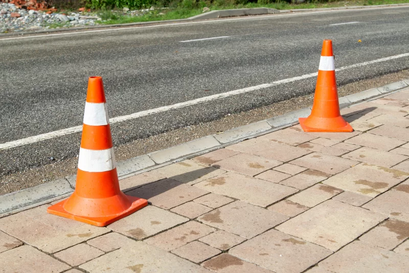 Два оранжевых дорожных конуса на тротуаре у асфальтовой дороги