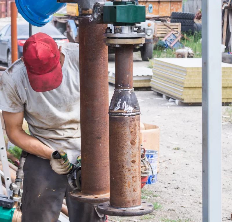 Рабочий обрабатывает металлическую трубу угловой шлифмашиной на стройплощадке
