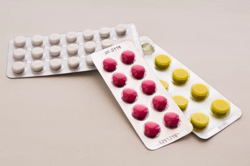 Упаковки таблеток: розовые, желтые и белые таблетки в блистерах на светлом фоне