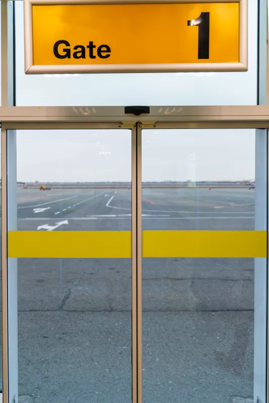 Автоматические двери аэропорта с указателем "Gate 1" и видом на взлетно-посадочную полосу