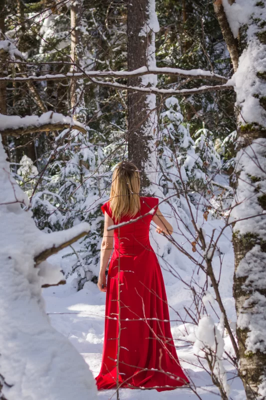 Женщина в красном платье посреди заснеженного зимнего леса