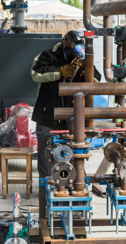 Рабочий-сварщик в защитной маске работает над трубопроводом