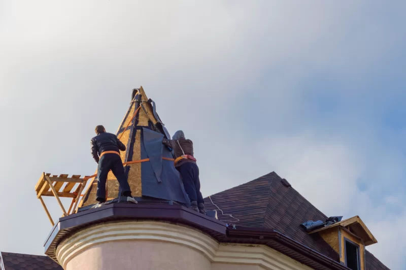 Рабочие устанавливают крышу на башне мансарды