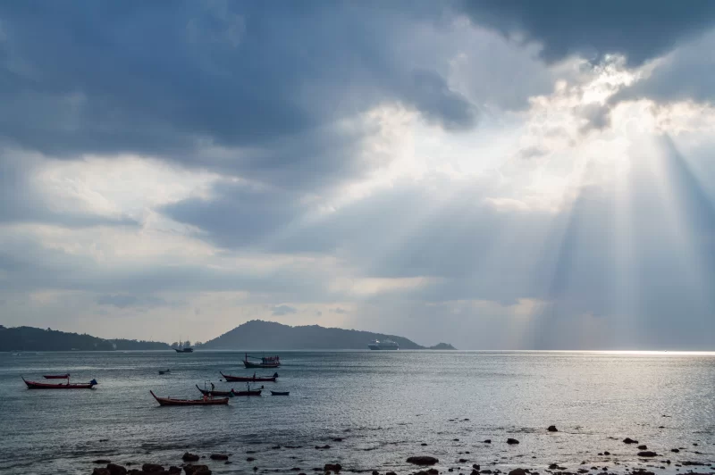 Солнечные лучи пробиваются сквозь тёмные облака над спокойным морем