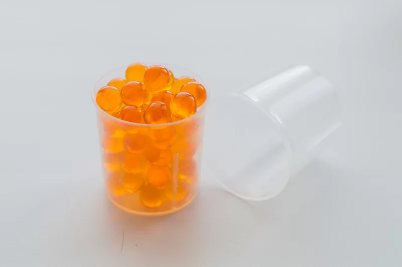 Яркие оранжевые шарики в мерном стаканчике на белом фоне