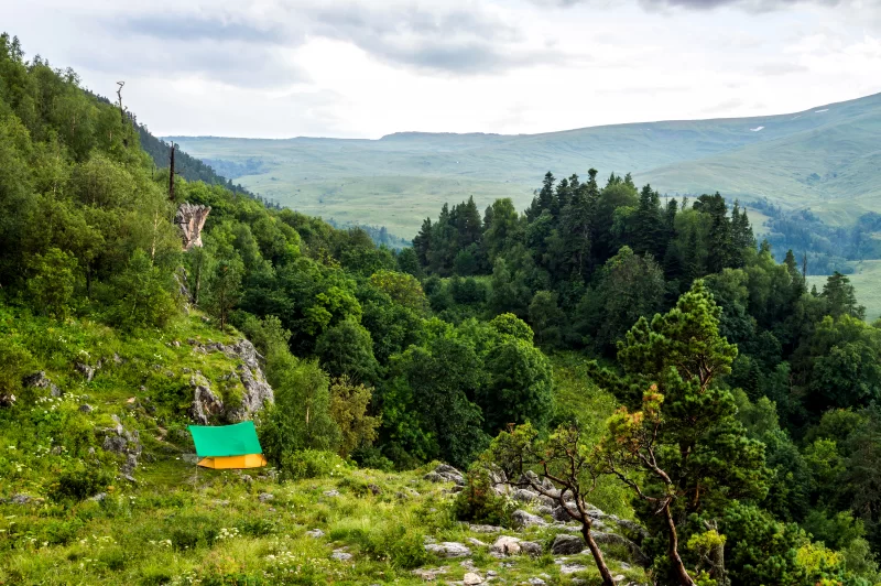 Кемпинг в горах с зелёной палаткой на травянистой склоне