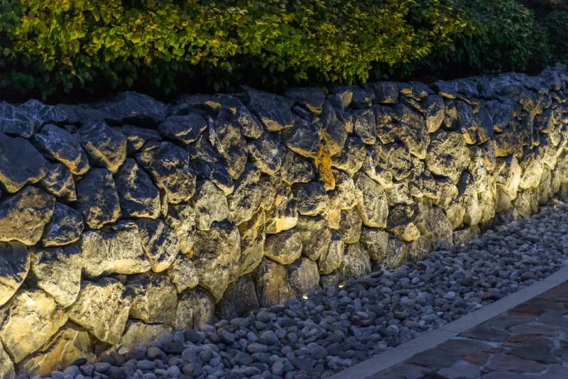 Подсвеченная каменная стена и сад