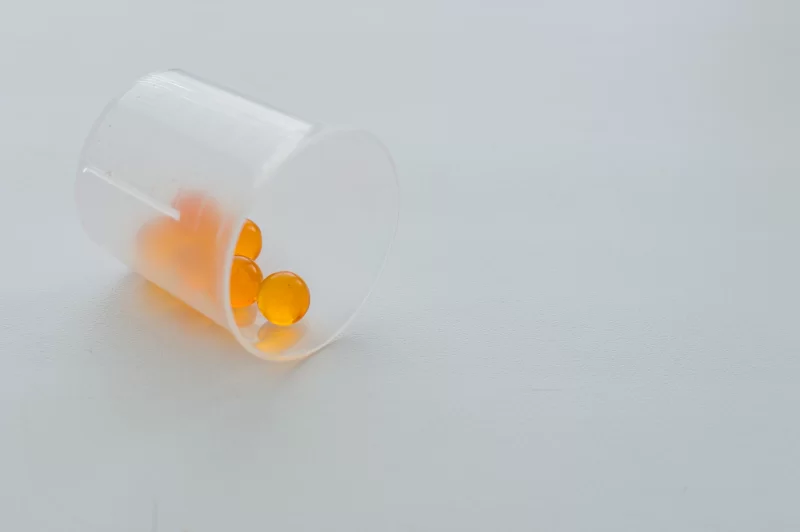 Прозрачный стаканчик с оранжевыми капсулами на светлом фоне