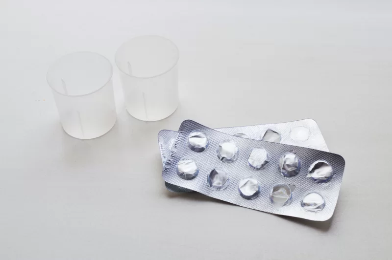 Пустые упаковки от таблеток и мерные стаканчики на светлом фоне