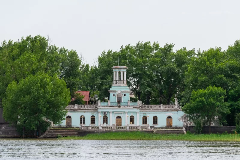 Старинное здание на берегу реки с густой зеленью