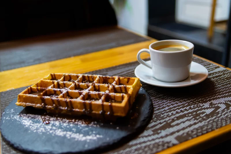 Аппетитный бельгийский вафля с шоколадным соусом и чашкой кофе
