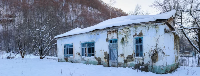 Заброшенный деревенский дом под снегом в зимнем лесу