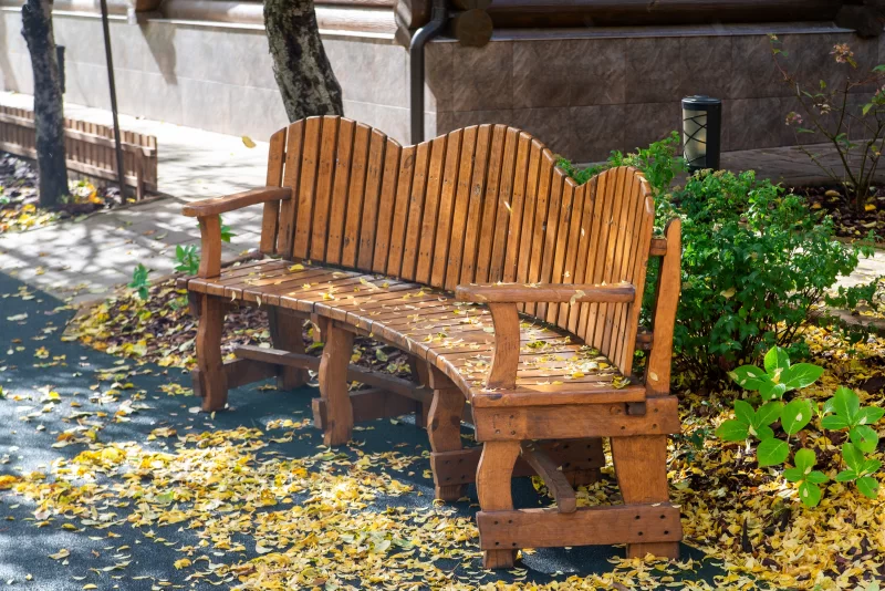 Деревянная скамейка в осеннем саду с падающими листьями