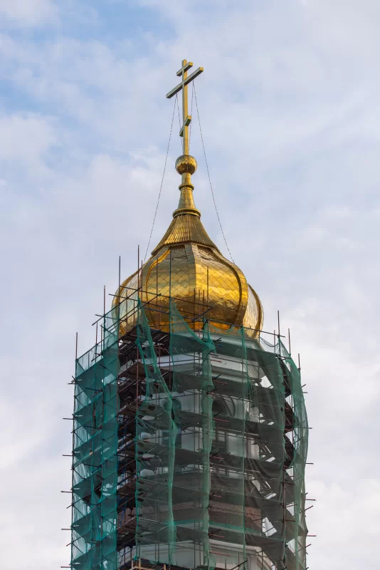 Золотой купол церкви под строительными лесами и сеткой на фоне неба