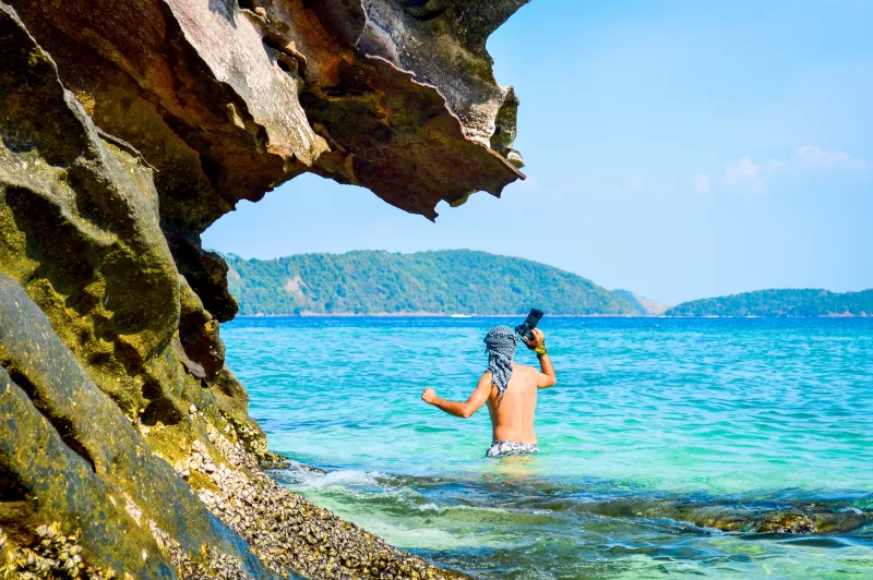 Фотограф в тропическом море под скалой