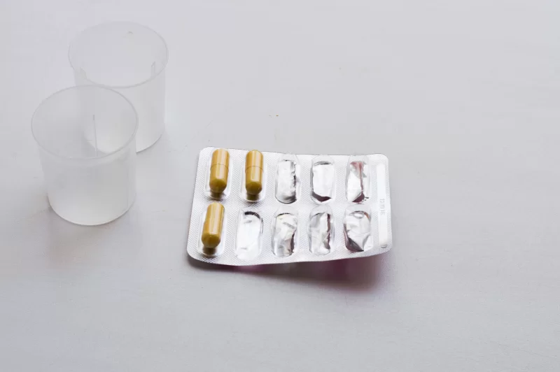 Лекарства в блистере и мерные стаканчики на сером фоне