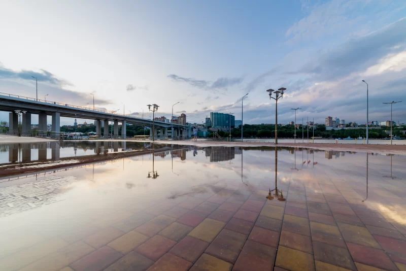 Отражение моста и неба в луже на городском речном тротуаре