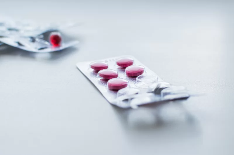 Блистер с таблетками и красные капсулы на светлом фоне