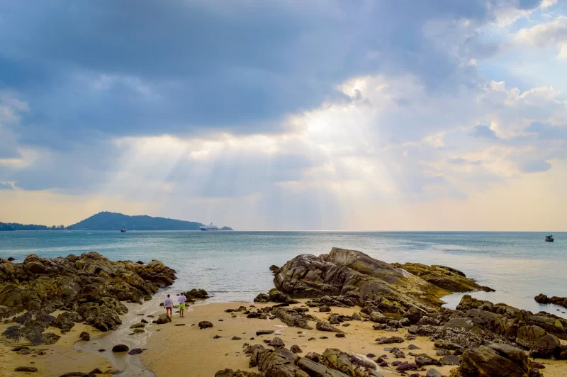 Golden sunset over rocky beach with two people walking